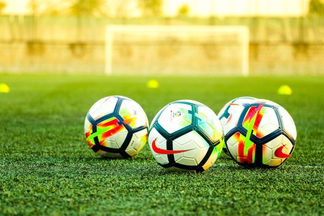 Drei Fußbälle liegen auf einem Kunstrasen vor einem Fußballtor