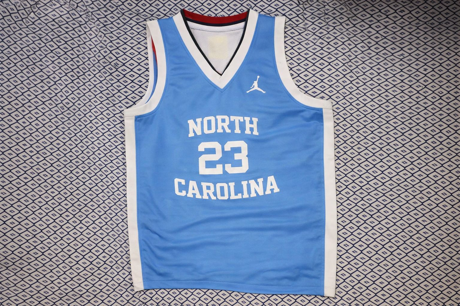 Hellblaues Basketball-Trikot der North Carolina mit der Nummer 23 auf gemustertem Hintergrund.
