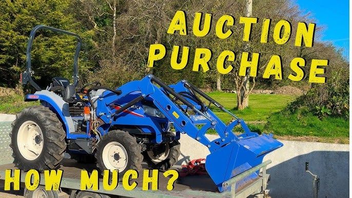 Ein blauer Iseki Kompakttraktor mit Frontlader steht auf einem Transportanhänger.